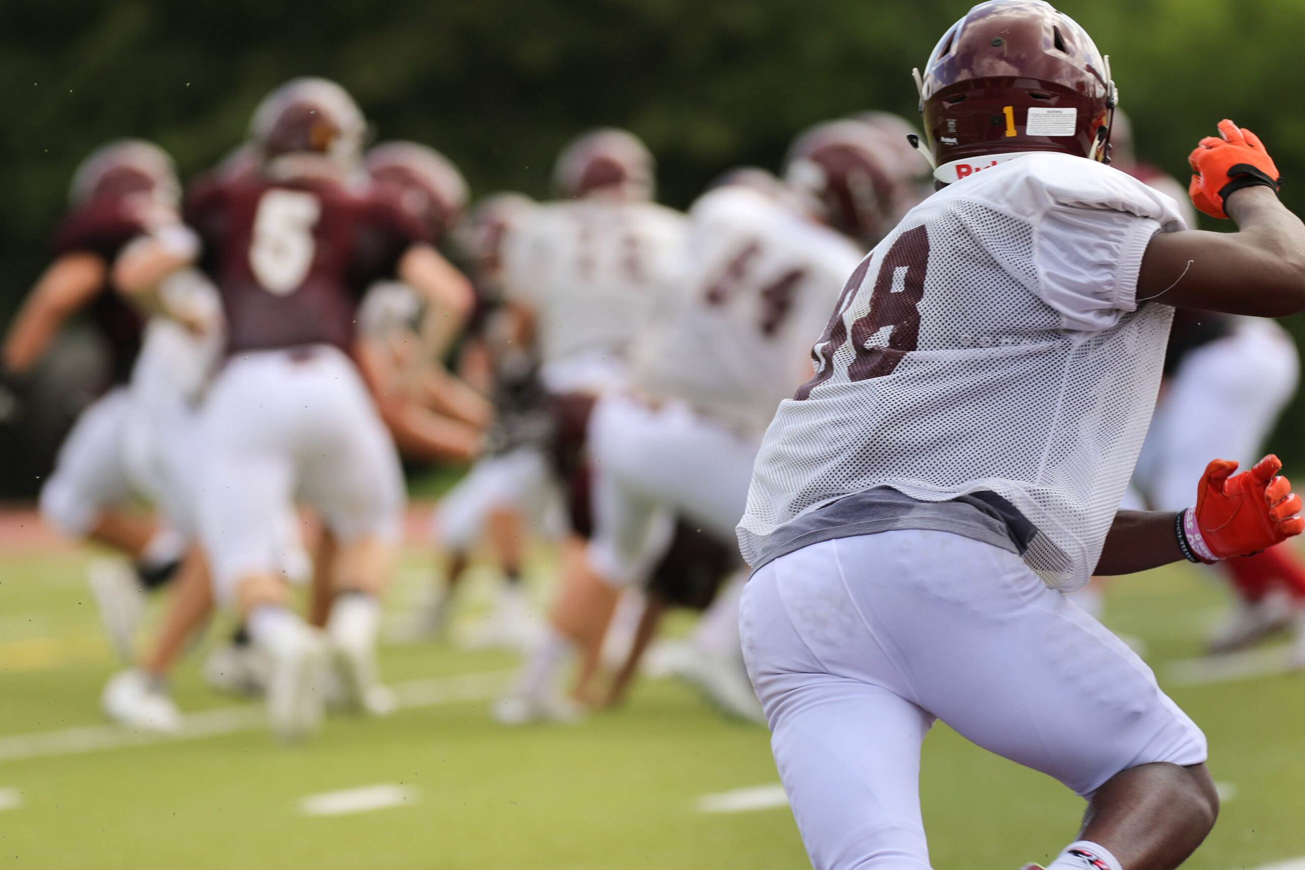 Football player in a non-contact jersey sprinting toward the play during practice, representing the high-speed cuts and collisions that sports massage in Billings Montana helps manage for field-sport athletes.