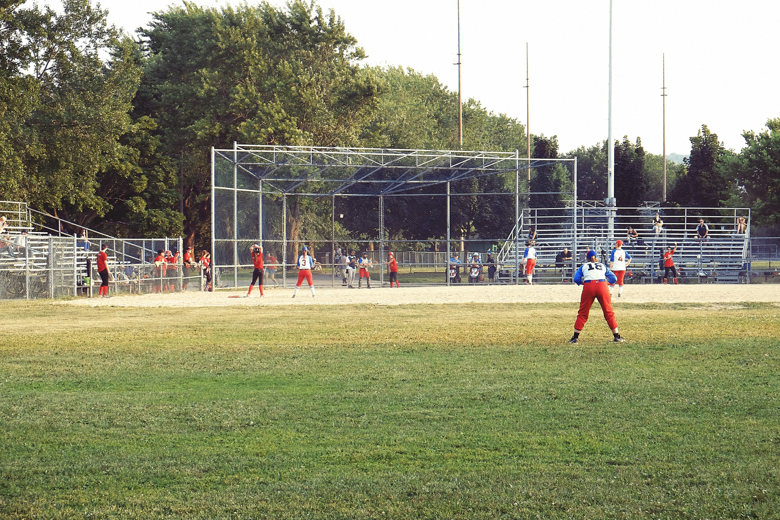 League softball players on a community field during a game, illustrating the throwing, batting, and sprinting demands that sports massage in Billings Montana helps address for arm, shoulder, and leg overuse.